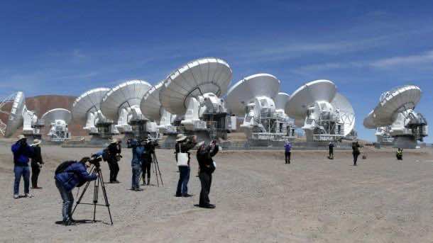 Members of the media work in front of the parabolic antennas of the ALMA project at the El Llano de Chajnantor in the Atacama desert