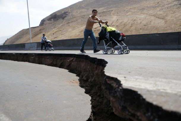 Residents push prams along a damaged road leading to Alto Hospicio commune after a series of aftershocks in Iquique