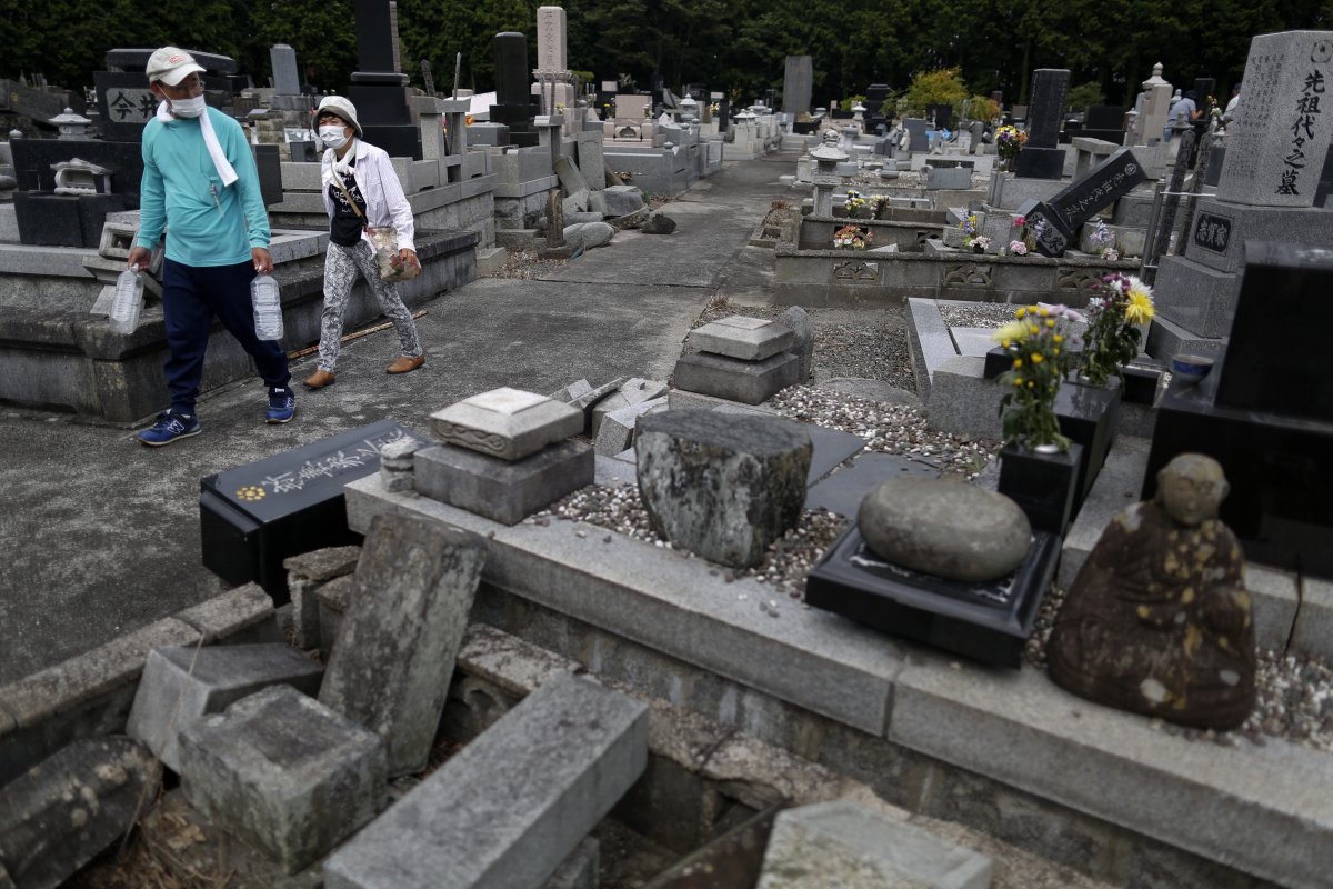 People wear face masks as they visit the graves of their relatives at a cemetery damaged by the earthquake in Tomioka.